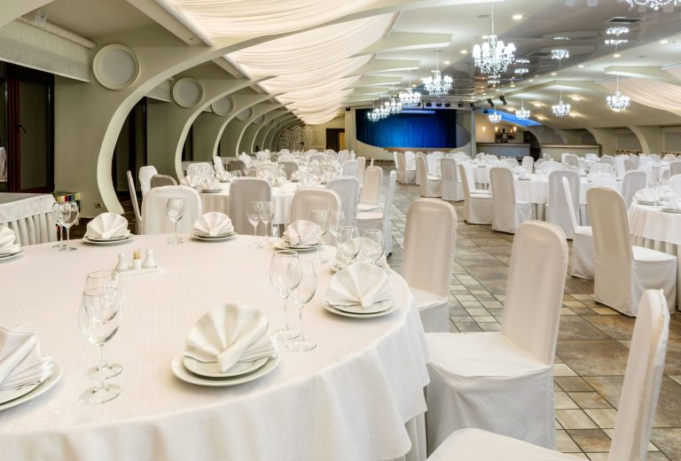 Banquet hall decorated in white with round served tables and sta